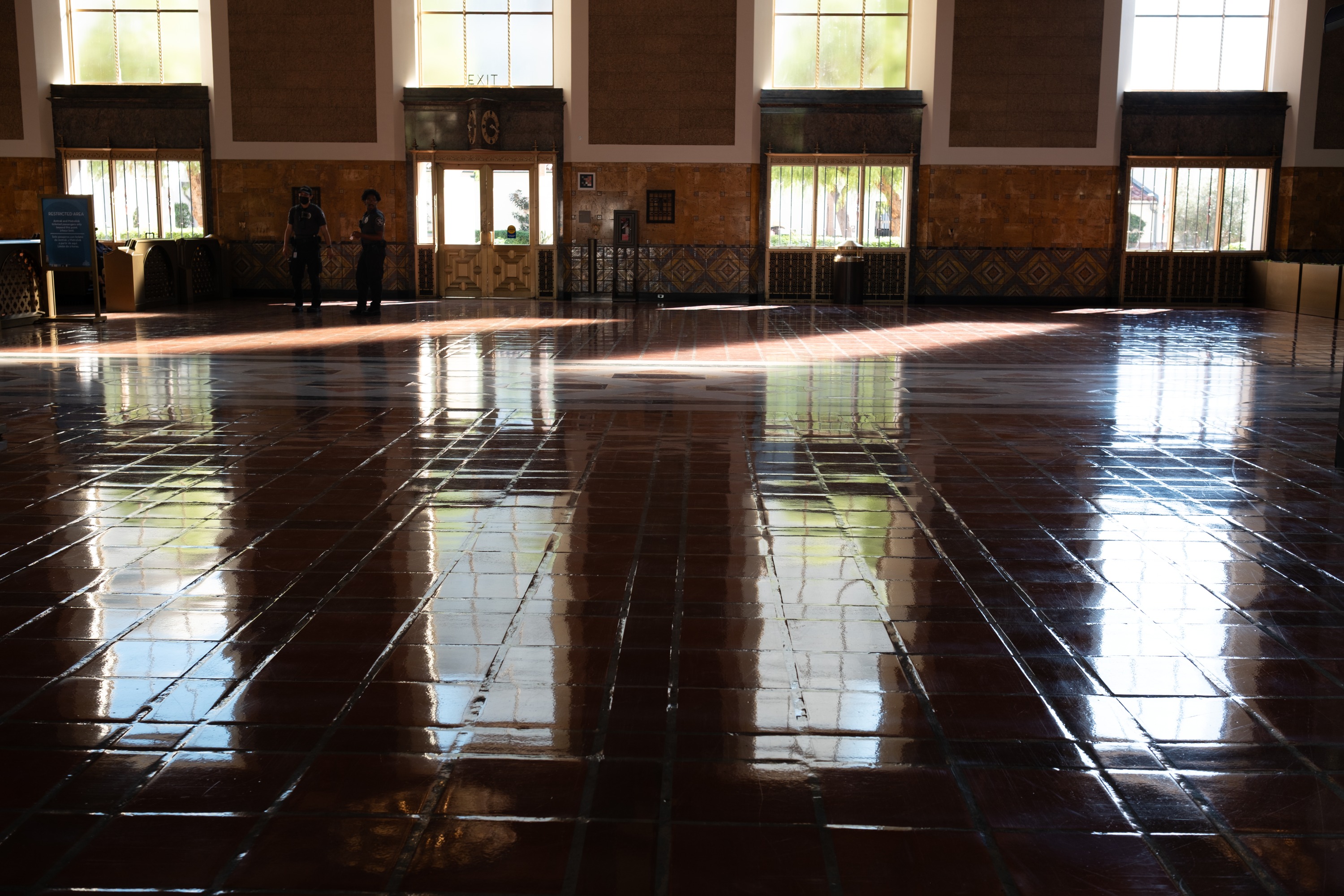 Two figures beside tall windows and sunlight reflected across the tiled floor of Los Angeles Union Station