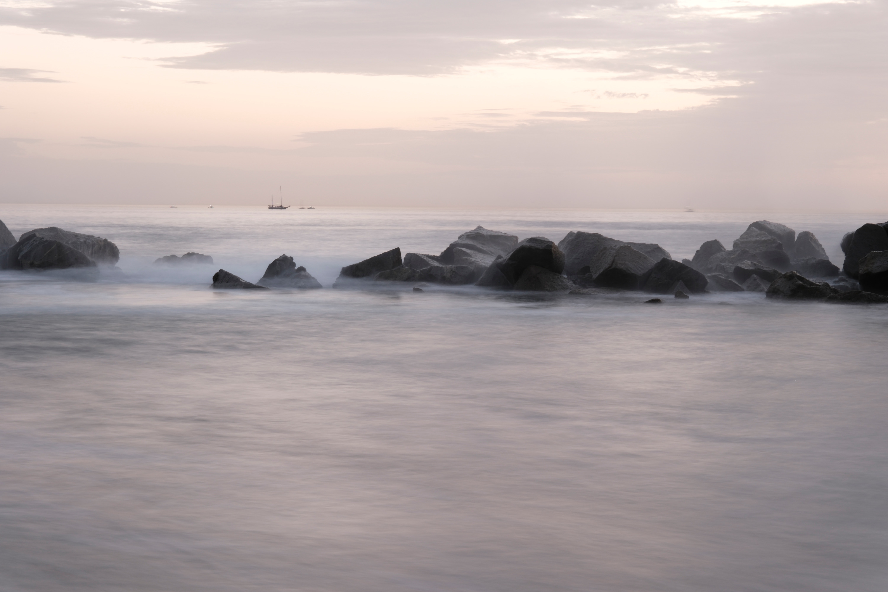 Jiho An photograph of rocks and softly flowing ocean water beneath a pale pink sky at Venice Beach, California